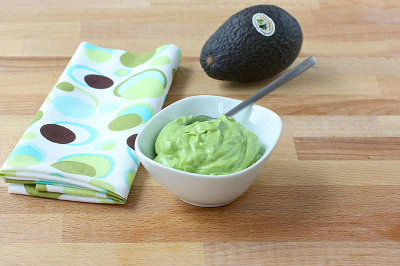 avo-sauce-in-dish-avo-in-backgrnd.jpg Bowl of avocado sauce next to a kitchen towel an a whole avocado