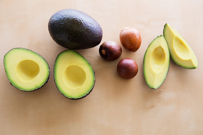 avocado-seed-3.jpg halved avocado next to a whole avocado, three pits, and two slices of avocado