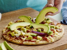 hand placing a slice of california avocado on the all american avocado pizza