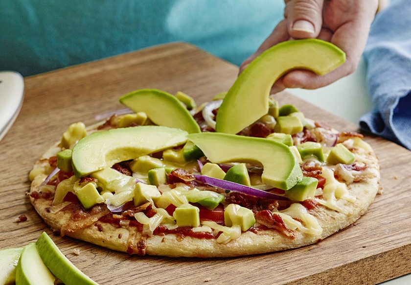 hand placing a slice of california avocado on the all american avocado pizza